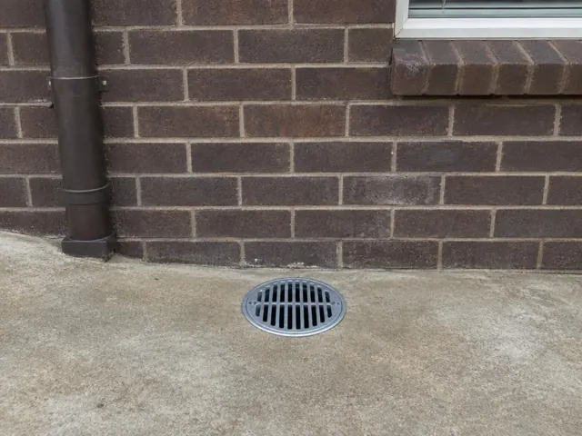 Outdoor gully grate in a concrete patio beside a brick wall and downpipe in Pymble